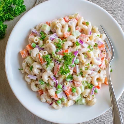 Chilled elbow macaroni tossed with crunchy vegetables and fresh herbs in a mayonnaise-based dressing, served in a white bowl.