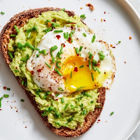 A close-up of two slices of avocado toast on a rustic plate, ready for breakfast with a cup of coffee nearby.