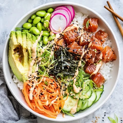 Fresh marinated salmon poke bowl with creamy avocado slices and crunchy vegetables on white sushi rice, drizzled with spicy mayo.