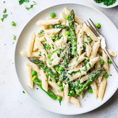Fork twirling a bite of Garlic Parmesan Spring Vegetable Pasta, showcasing tender vegetables and a light, creamy garlic-parmesan sauce on a rustic wooden table.  