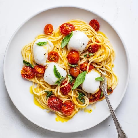 Close-up of Burrata Caprese Pasta on a white plate, showcasing torn burrata cheese melting into the warm pasta and tomatoes. 