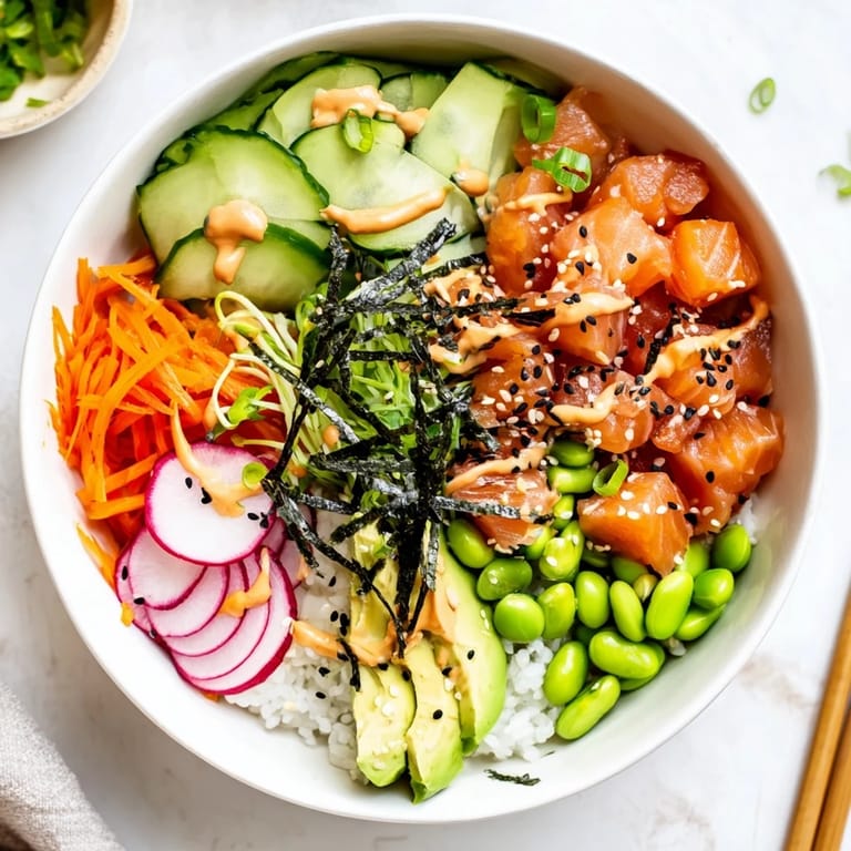 Colorful Hawaiian-inspired poke bowl featuring diced tuna, cucumber, edamame, and carrots, topped with sesame seeds and nori strips.