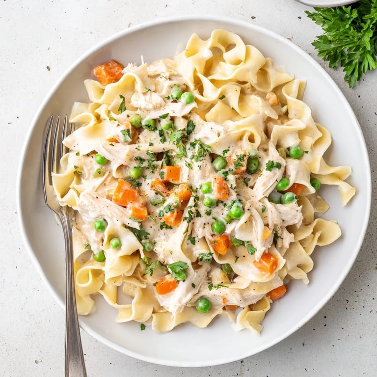 A family-friendly Spring Chicken Noodle Skillet features golden noodles, shredded chicken, and peas in a light, Parmesan cream sauce.