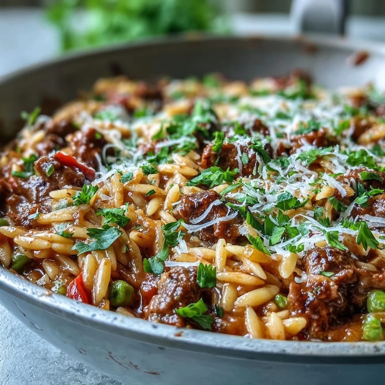 A bubbling skillet of Comforting Ground Beef Orzo Dinner with melted Parmesan, fresh parsley garnish, and steam rising from the saucy pasta.